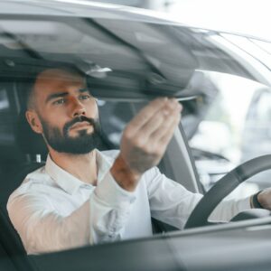 Inside of the automobile. Young man in white clothes is in the car dealership
